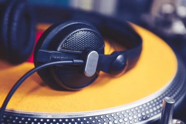 Professional DJ headphones laying on yellow clipmat on turntable vinyl records player.Turntables platter in focus,no record.Pro analog audio equipment