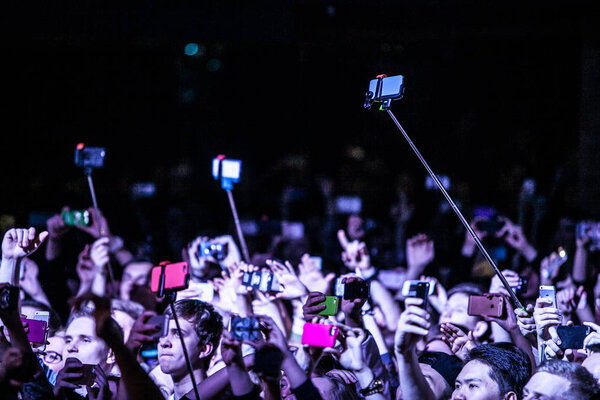 MOSCOW - 27 MARCH,2015: Music fans filming concert with mobile phones on selfie sticks.Popular gadget for smartphone.Crowded dance floor in the club.People take photos on concert