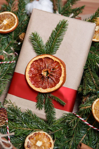 Decorative brown paper gift package with red ribbon,dryed orange fruit slice,fir tree branch.Close up,vertical shot.Decorate your Christmas and New Year gifts for friends and family