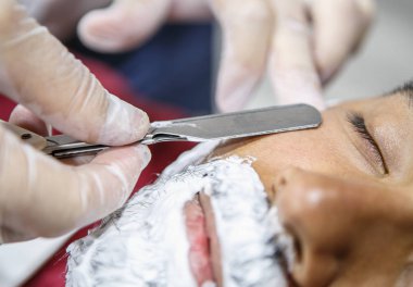 Kuaför keskin usturalar tıraş makinesi aracıyla yeni sakal şekli genç siyah adam yüzünde keser. Erkek güzellik tedavi kavramı