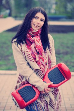 Esmer beyaz girll modern kırmızı elektrikli mini segway ya da vurgulu kurulu scooter parkta yürürken elinde tutan. Popüler yeni becerikli alet. Kız trendy boho tarzı kıyafetler giyiyor.