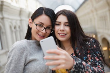 Selfie büyük modern gümüş akıllı cep telefonu ile alışveriş merkezinde alarak iki çekici genç kadın. Mutlu beyaz kızlar, yeni smartphone aygıtı