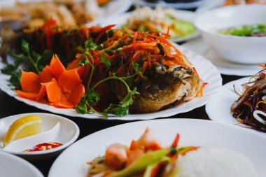 Geleneksel Vietnam salata ve deniz ürünleri ile baharatlı kızarmış karp balık görüntüsünü kapatın. Büyük Asya Restoran akşam yemeği. Karides rulo, yılan balığı salatası ve pho bo çorba servis Çin kafede masada. Balık üzerinde odaklanmak