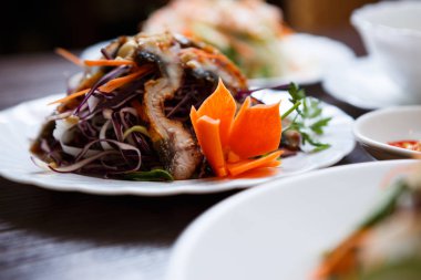 Egzotik Vietnam gıda restoran menü kapatın. Geleneksel Asya yemeği beyaz tabakta. Yılan balığı salatası taze sebze balık deniz ürünleri ve kırmızı lahana