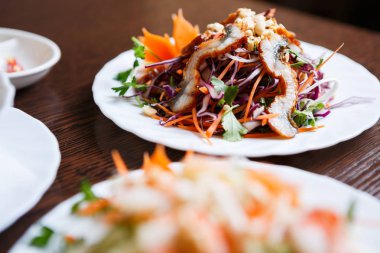 Egzotik Vietnam gıda restoran menü kapatın. Geleneksel Asya yemeği beyaz tabakta. Yılan balığı salatası taze sebze balık deniz ürünleri ve kırmızı lahana