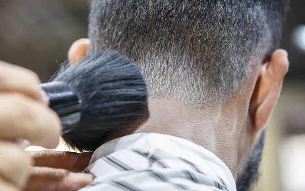 Young black man client getting new haircut in barbershop.Barber hairdresser spreads powder on clients neck with professional shaving brush before cutting hair with razor.Male beauty treatment concept