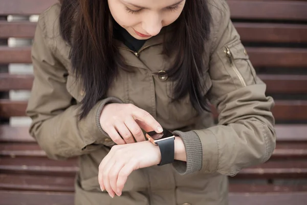 Young hipster girl in parka coat using her smart watch. This new gadget lets you always stay connected to internet and social media networks from anywhere you want.