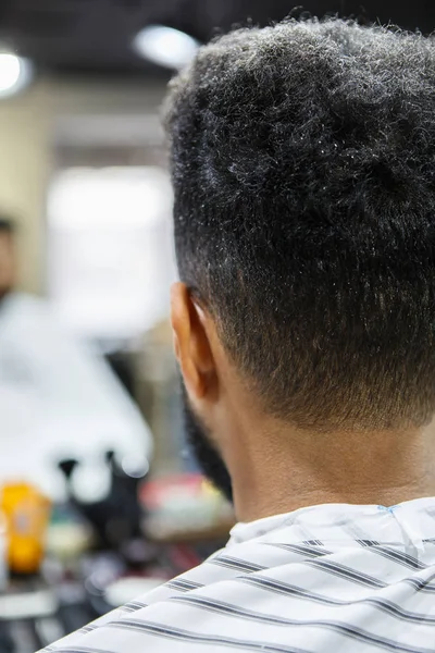 Unshaven young black man in barbershop.Cut nape hair and trim beard in professional barber shop salon.Male beauty treatment process background.