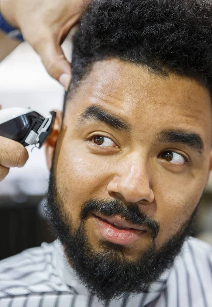 Portrait of young black man in barbershop.Handsome African guy makes new haircut in barber shop salon. Male beauty treatment process in close up