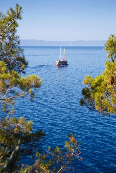 Tourist boat swim on waves of deep blue Adriatic Sea in Croatia.Beautiful seaside view from mountain top.Vertical seascape with big motor boat carrying tourists for cruise to exotic islands in Europe