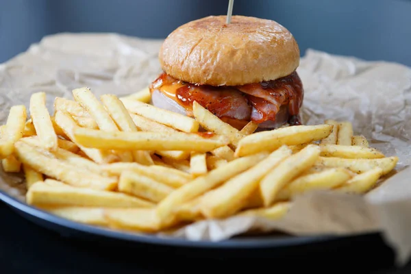 Delicious big fat crafted hamburger served on brown decorative paper in fast food restaurant menu.Tasty,but unhealthy junk food with fat meat,sauce & French fries on plate in cafe