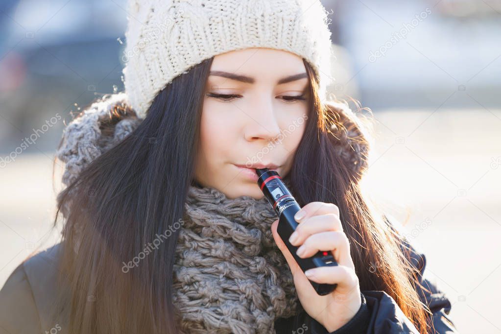 Cute young white girl vape outside.Popular electronic gadget for vaping ejuice or eliquid.Modern portable electronic cigarette in use.Young woman with e-cig vaporizer device