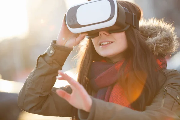 モバイル ゲーム用の最新のバーチャルリアリティ眼鏡と遊ぶ若い女の子 革新的な ヘッドセットと携帯アプリを使用します ヘッド セット冬の日没で屋外で女遊び — ストック写真