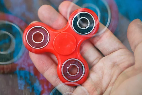 Super popular red spinner device in male hand.Guy holding fidget gadget in hands.Modern spinning toy for youth & adults.Learn cool new tricks & have fun.Red object,blue background