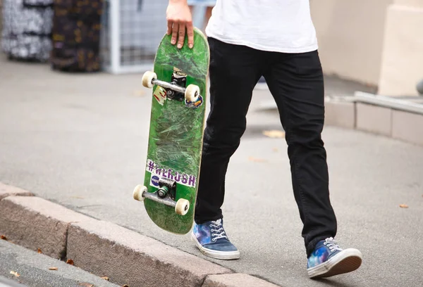 KIEV - 21 JULY, 2018: Cool young skater boy walking down the street with old skate board deck in hands. Extreme summer sports background. Feet of teenager skateboarder athlete