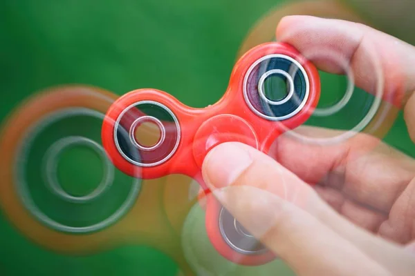 Red spinner fidget device in hand.Guy playing with awesome new spinning toy.Enjoy this cool new balance game & learn new tricks.Super popular gadget with bearings in the middle