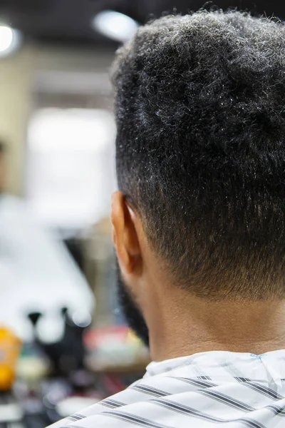 Unshaven young black man in barbershop.Cut nape hair and trim beard in professional barber shop salon.Male beauty treatment process background.