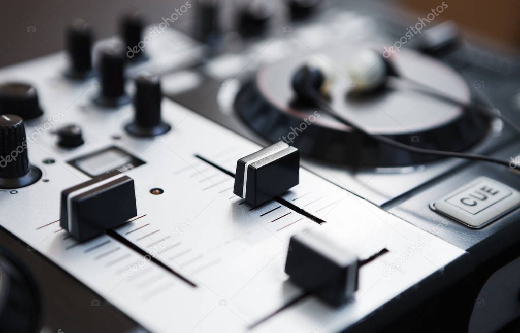 Sound mixer and midi controller for DJ. Focus on volume faders, deck platter and headphones on background. Play your music