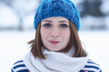 Funny young ginger girl making faces.Blurred background.Beautiful young white girl in warm blue knit winter hat posing outdoor.Winter blurry background out of focus.Place text over blur backdrop 
