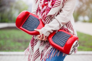 Kadın modeli modern kırmızı elektrikli mini segway ya da vurgulu kurulu scooter parkta yürürken elinde tutan. Hava kirliliği atmosfere üreten popüler yeni ulaşım teknolojisi. Kız gidişli boho tarzı kıyafetler giyiyor.