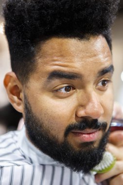 Berber içinde oturan tıraşsız genç siyah adam portresi Kuaför onu yeni şık saç ve sakal ve bıyık saç kesim yapmak bekleyen battaniye ile kaplı. Erkek güzellik tedavi kavramı