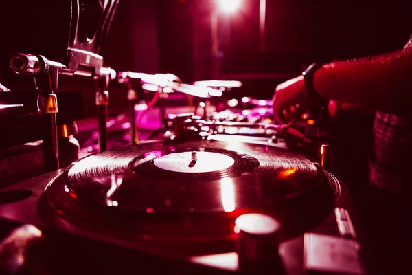 KIEV-4 JULY,2018: Technics SL 1210 turntable player with old analog vinyl record disc on concert stage in bright red lights.Disc jockey plays musical tracks on techno party event.Profesional djs setup