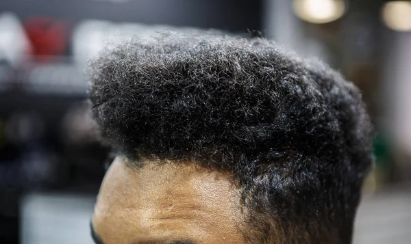 Unshorn hair of young black man in barber shop.Close up curly locks of unshaven African guy in barbershop salon.Male beauty treatment concept