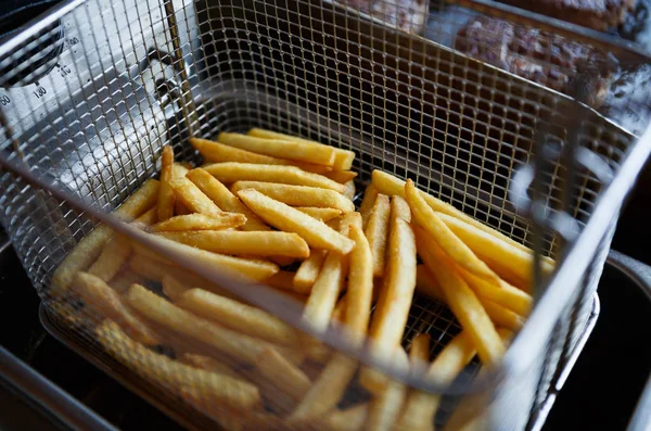 French fries boiled in hot oil on kitchen.Tasty but so bad & unhealthy food in American restaurant.Close up on oily fried sliced potatoes in metal cage.Junk food cookin