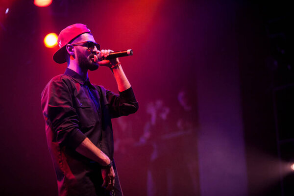 MOSCOW - 20 OCTOBER, 2016 : Rap singer sing on stage of night club. Hip hop music performer singing in microphone on stage. Rapper in bright concert lighting.