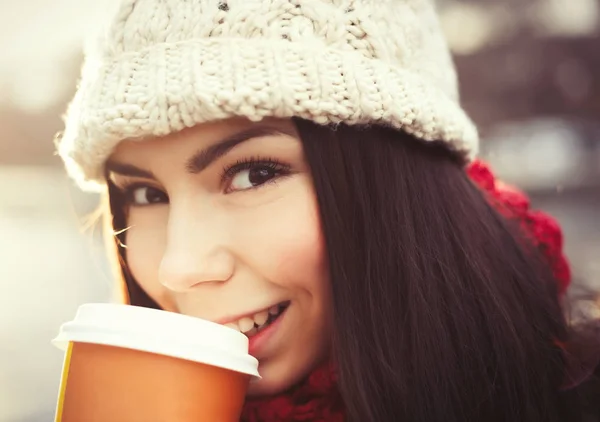 暖かい冬の服でブルネットの女の子は寒い日に屋外でホットコーヒーを飲みます 魅力的で幸せな若い女性の明るいバックライト付き肖像 — ストック写真