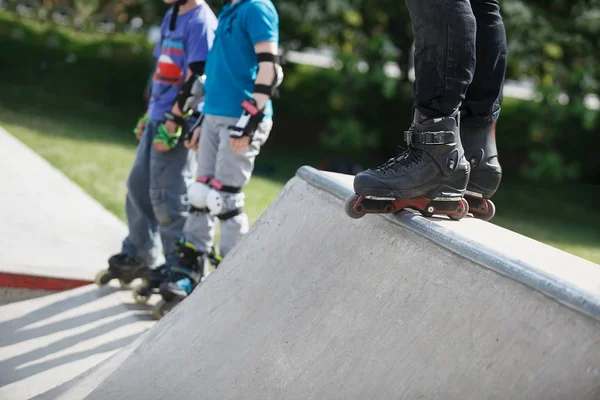 屋外のスケート公園でコンクリート製の傾斜の上に立って積極的なインライン スケートを着てローラーブレードを楽しむ人の足 極端なスポーツ選手のトリックやグラインドのローラーブレードを着用 — ストック写真