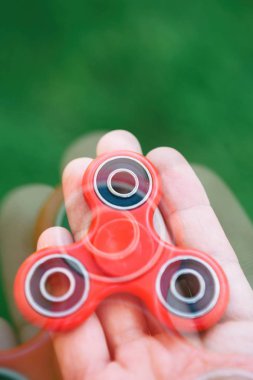 Spinner kıpır aygıtı elinde. Adam tutmak yatakları ile modern kırmızı iplik oyuncak. Serin yeni denge püf noktalarını öğrenmek ve bu popüler cihaz ile eğlenin. Birght yeşil arka plan, odak üstünde becerikli alet