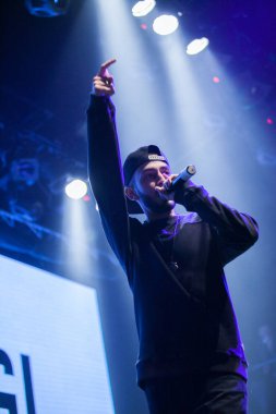 MOSCOW - 20 OCTOBER, 2016 : Rap singer sing on stage of night club. Hip hop music performer singing in microphone on stage. Rapper in bright concert lighting. clipart