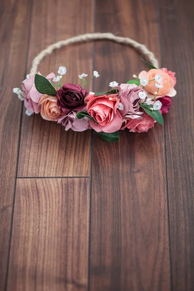 Handmade wraith or diadem made of pink and red rose flowers lying on the wooden surface. Shallow depth of field, macro close up, copy space on the bottom