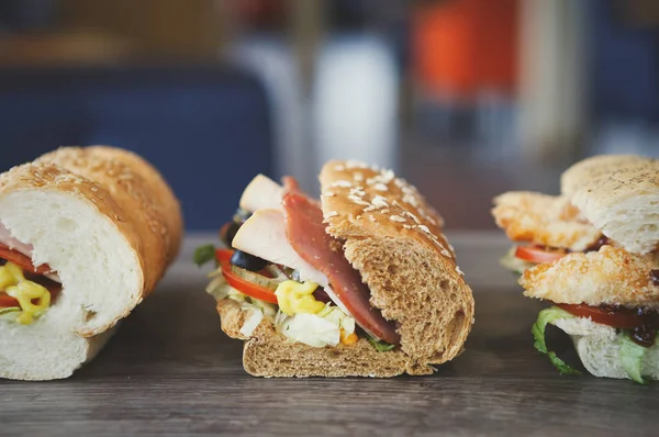 Three delicious sandwiches on table in cafe.Fast food restaurant menu.Sandwich snacks close up.Fresh vegetables & meat in sauce.Fastood cafe background