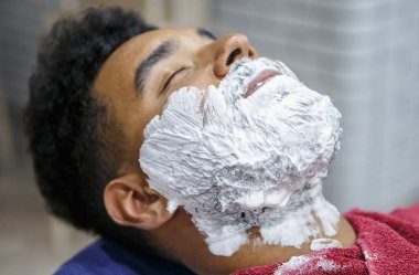 Berberde tıraş için yüzünde beyaz köpük genç siyah adam portresi. İstemci sakal üzerine krema ile. Erkek güzellik tedavi kavramı