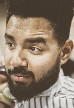 Berber içinde oturan tıraşsız genç siyah adam portresi Kuaför onu yeni şık saç ve sakal ve bıyık saç kesim yapmak bekleyen battaniye ile kaplı. Erkek güzellik tedavi kavramı