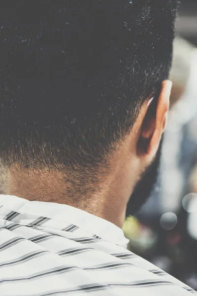 Back of the head and nape of young African man in barbershop. Male beauty treatment process in barber shop.Black guy covered with blanket cuts his hair in salon