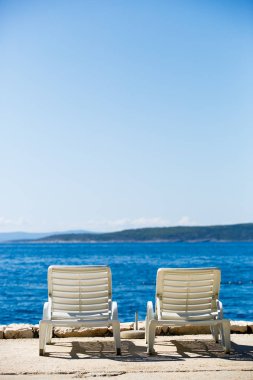Lüks Avrupa plajında, arka planda açık mavi deniz suyuyla iki beyaz plastik güneşlik. Yaz tatili turu için seyahat yeri. Rahatlamak ve rahatlamak için Akdeniz kıyısına seyahat edin.