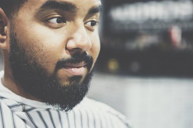 Tıraşsız genç siyah erkek berber koltuğunda oturmak portre Kuaför Kuaför saçını kendi kesecek ve bıyık ve sakal trim bekleyen battaniye ile kaplı. Erkek güzellik tedavi kavramı