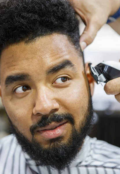 Portrait of young black man in barbershop.Handsome African guy makes new haircut in barber shop salon. Male beauty treatment process in close up