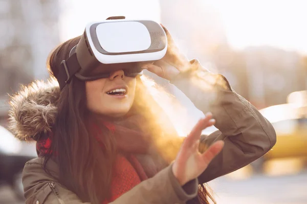 Young female play with super cool virtual reality glasses for mobile gaming applications outdoor in sunset.Use mobile apps with innovative vr headset.Trendy augmented reality gamer gadget in use