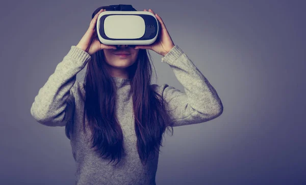 Studio portrait of young brunette girl playing with virtual reality goggles for mobile game application.Girl use mobile games apps with innovative 3d vr headset.Trendy augmented reality gadget in use