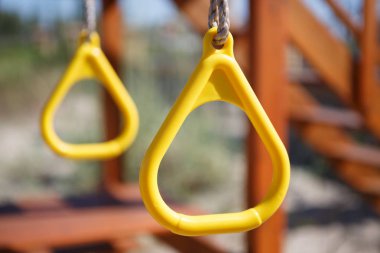 Yellow monkey bars on children playground in sunny summer day. Fun outdoor activity for kids. Swing on hanging plastic rings outside 