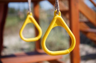 Yellow monkey bars on children playground in sunny summer day. Fun outdoor activity for kids. Swing on hanging plastic rings outside 