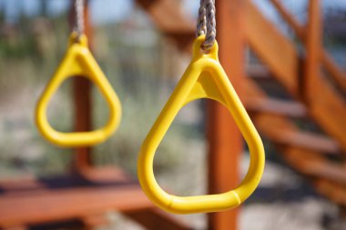 Yellow monkey bars on children playground in sunny summer day. Fun outdoor activity for kids. Swing on hanging plastic rings outside 