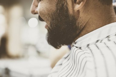 Genç berber koltuğu yeni saç kesimi yapmak ve bıyık trim Kuaför için bekleyen oturuyor ve tıraşsız sakallı adam siyah. Erkek güzellik salonu tedavi sürecinde