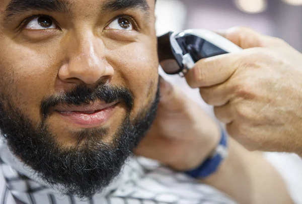 Portrait of black man getting new haircut in barbershop.Handsome African guy being trimmed with clipper machine in barber shop salon.Male beauty treatment process in close up