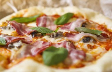 Italyan kafede lezzetli pizza. Italya 'da gelenek yemek görüntüleri, Yeşil fesleğen yaprakları, siyah zeytin, yanmış peynir ve pastırma dilim ile pişmiş hamur tabanı.