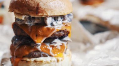 Lezzetli büyük şişman duble hamburgerin görüntüleri. Amerikan Fast food restoran menü çanak. Sos ile ızgara büyük Burger, domuz ve yakıcı peynir kafede kahverengi kağıt üzerinde hizmet vermiştir. Hızlı yiyecek video yakın çekim.